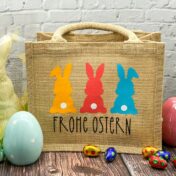 Jutetasche mit aufgedrucktem Spruck "Frohe Ostern" und drei bunten Osterhasen mit weisser Quaste